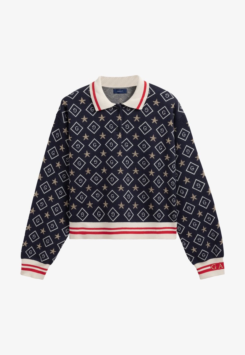 Granatowy krótki pulower z kołnierzykiem polo, zdobiony wzorem w diamenty i gwiazdy w złotym kolorze. Czerwono-białe paski na dolnej krawędzi i mankietach.