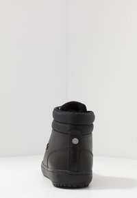 Czarny botek za kostkę z błyszczącym skórzanym wykończeniem, pikowanym mankietem i teksturowaną podeszwą. Z tyłu ozdobiony okrągłym logo.