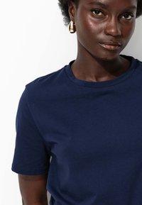 T-shirt à manches courtes bleu marine avec un col rond, texture de tissu lisse et finitions de couture soignées. Aucun motif ni logo visible.