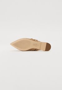 Scarpa in suede beige con punta a punta e tacco affusolato, caratterizzata da cinture incrociate testurizzate sulla parte superiore e una suola liscia.