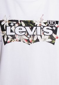Bílý bavlněný tričko s květinovým logem Levi's v černé a živých barvách, obklopené bílými a růžovými květinami a zelenými listy.