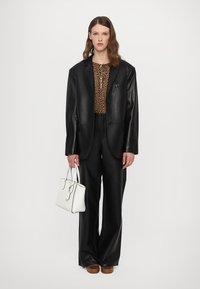 Čierny kožený oversize blazer na leopardom topu, kombinovaný s čiernymi nohavicami s vysokým pásom a bielou kabelkou. Hnedé platformové topánky.