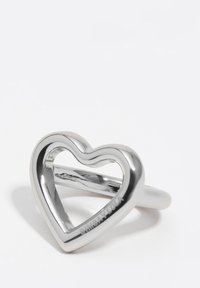 Anillo de plata con forma de corazón, con centro hueco, superficie lisa y acabado pulido. Marca distintiva en un lado.