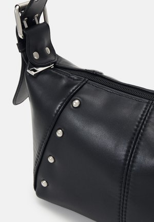 Sac à bandoulière en cuir noir avec clous argentés, fermeture à glissière et bandoulière réglable à boucle, sur fond blanc.