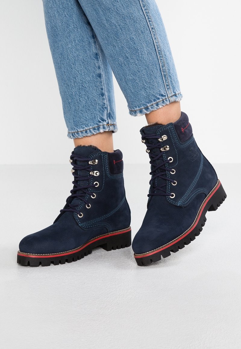 Marinblå mocka ankelstövlar med rund tå, metallöglor, röd detalj nära sulan och svart grov sula för bättre grepp.