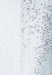 Shimmering fabric with silver sequins in various sizes, arranged closely on a light blue background, giving a textured, reflective appearance.