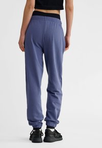 Paarse joggingsbroek van zachte stof met een elastische tailleband en boorden; gecombineerd met zwarte sportschoenen met een textuurontwerp.