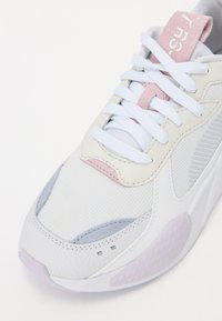 Witte sneaker met een mix van texturen, waaronder mesh en leer, met pastelkleurige accenten in roze en lichtblauw, en platte witte veters.