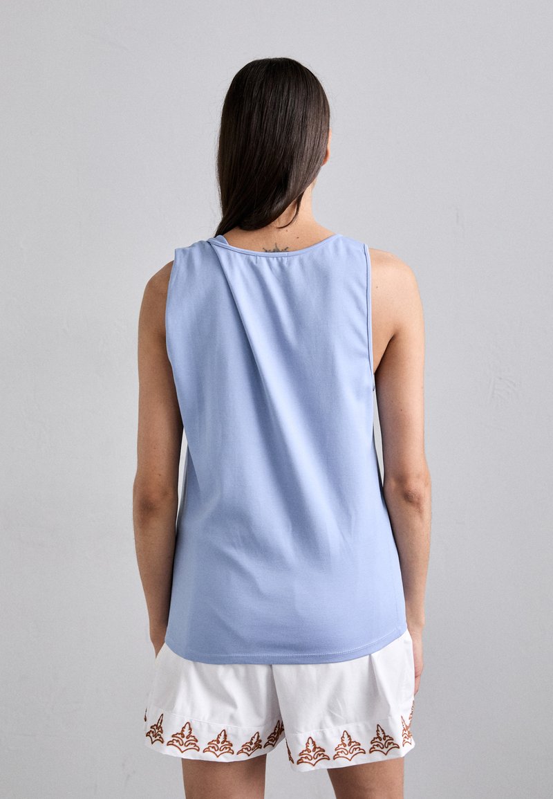 Lichtblauwe mouwloze top met een ronde halslijn. De stof lijkt zacht, met een gladde textuur en een ontspannen pasvorm aan de achterkant.
