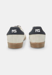 Fehér vászon sportcipők sötétkék sarokkal. Gumi talp textúrált felülettel. A saroknál logóval és minimalista dizájn elemekkel rendelkezik.