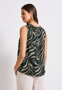Top senza maniche di un verde scuro con un motivo ondulato beige e marrone chiaro. Presenta un colletto arricciato e una vestibilità comoda.