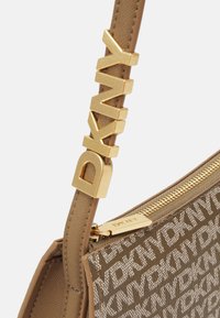 DKNY crossbody bag in light brown fabric with embossed logo pattern, gold hardware, and a textured strap featuring the brand name.