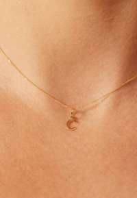 Collier en or avec une chaîne fine et un petit pendentif en forme de "C" cursif, présentant une finition lisse et un travail délicat.
