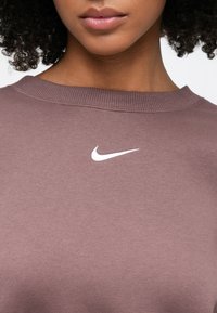 Μωβ φούτερ με ριμπ κοντή λαιμόκοψη και λευκό λογότυπο Nike στο στήθος. Το ύφασμα φαίνεται μαλακό με ομαλή υφή.