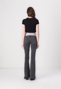 Camiseta negra de corte cropped combinada con unos jeans oscuros de tiro alto y acampanados. Los jeans cuentan con un dobladillo sin terminar y dos bolsillos traseros.