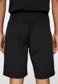 Svarta atletiska shorts med en slät yta, elastisk midja och knälång längd. Inga synliga logotyper eller mönster.