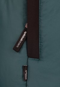 Teal stof met een textuurpatroon, voorzien van zwarte accenten en labels met de tekst "spitzbud studios." Stikwerk zichtbaar langs de randen.