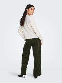 Off-white trui met een golvende zoom en lange mouwen, gecombineerd met donkergroene fluwelen wijd uitlopende broek. Zwarte pumps met puntige neus.