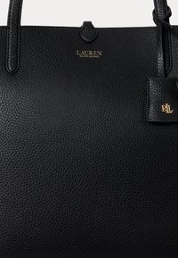 Čierna kožená taška typu tote s textúrou so zlatým logom "Lauren Ralph Lauren" a pripevnenou koženou visačkou s reliéfnymi zlatými iniciálmi "RL".