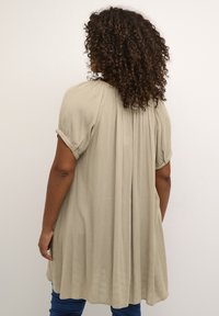 Blusa verde salvia a maniche corte con plissé sulla schiena, realizzata in tessuto leggero. Maniche arrotolate con dettaglio in bottone.