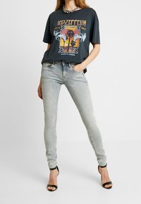 Camiseta gráfica negra con un diseño de Led Zeppelin, combinada con jeans skinny gris claro y tacones negros con tiras. Acabado con un collar de cadenas.
