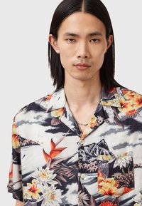 Camicia a maniche corte con stampa floreale, fondo nero, motivi tropicali vivaci e taschino sul petto; realizzata in tessuto leggero, design con bottoni.