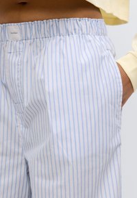 Ριγέ παντελόνι σε ανοιχτό μπλε και λευκό ύφασμα. Διαθέτει ελαστική μέση, πλαϊνή τσέπη και μαλακή υφή. Ορατό το λογότυπο της Calvin Klein.