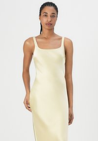 Satin glidelås kjole i lys gul med firkantet utrigning og tynne stropper, med en elegant, tettsittende silhuett og glatt tekstur.