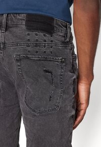Svarta slitna denimjeans med en texturerad finish, synlig fickstickning och fransade detaljer på bakfickan och midjebandet.