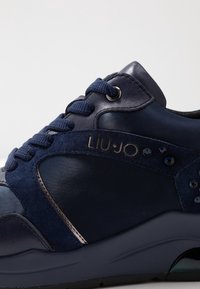 Marinblå sneakers i slätt läder och mocka, rund tå, blå snören, metalliska detaljer och dekorativa nitar på sidan.