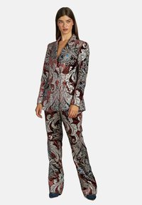 Velours pak met een rood en zilver paisley patroon. Heeft een blazer met notch-lapel en flared broeken, geaccentueerd met blauwe bloemmotieven.