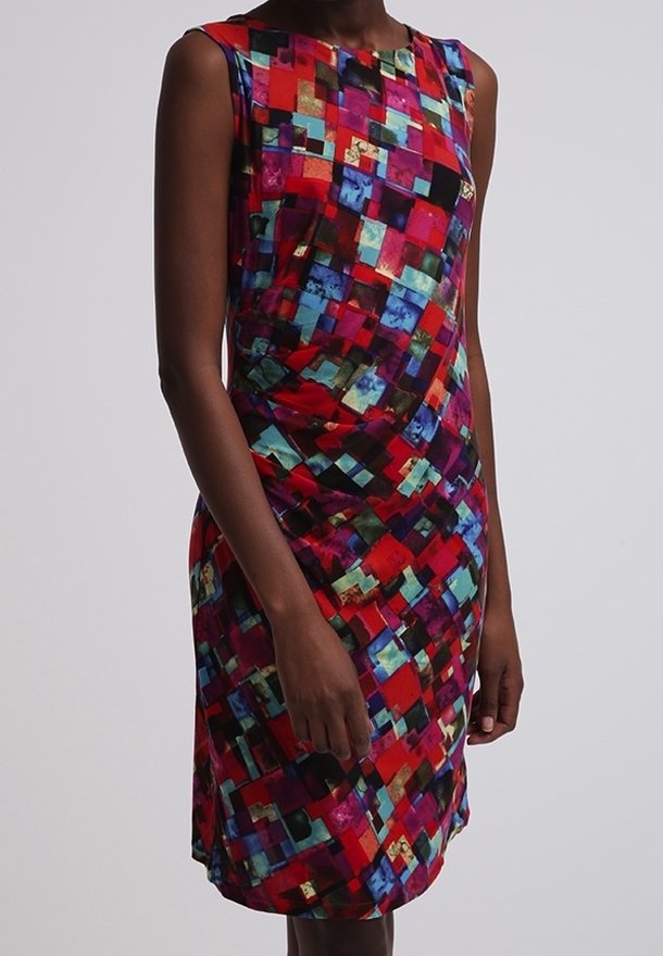 Femme portant une robe sans manches, longueur genou, à motif géométrique carré audacieux rouge, bleu et multicolore, posant devant un fond uni.