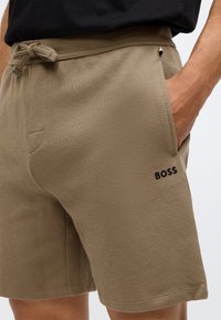 Pantaloni scurți bej, texturați, cu un model în carouri, ce prezintă un logo „BOSS” negru, buzunare laterale și o talie cu șnur.