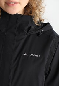 Giacca nera impermeabile con colletto alto, dotata di una chiusura a zip davanti, cappuccio regolabile con cordino e logo "Vaude" ricamato sul petto.