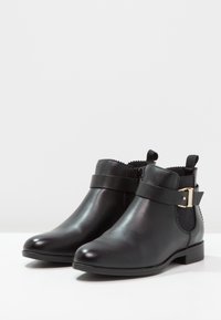 Black leather ankle boots with a rounded toe, side buckle detail, elastic side panels, and a low block heel. Smooth texture and classic design.