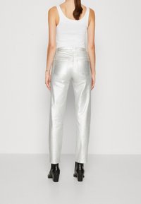 Pantalones metálicos plateados con diseño de pierna recta, dos bolsillos traseros y una cintura de altura media. Combinados con botas de tobillo con tacón negras.