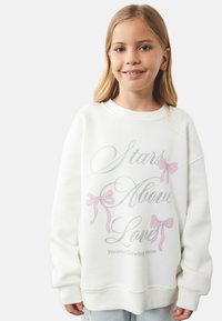 Biała bluza z różowymi grafikami kokard i srebrnym napisem "Gwiazdy ponad miłością". Posiada luźny krój i ściągacze przy mankietach.