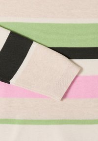 Manche de pull beige en tricot reposant sur un tissu en tricot rayé avec des bandes horizontales vertes, noires, roses et beiges.