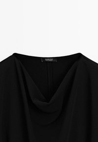 Blusa nera con scollo a cowl, realizzata in tessuto morbido. Presenta un'etichetta discreta sul retro, assicurando un'estetica minimalista.