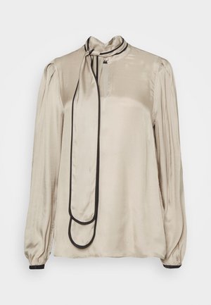 Saténová blůza ve světlém béžovém odstínu s vysokým límcem a černým lemem. Má dlouhé rukávy, přední knoflík a dekorativní uzel na límci.