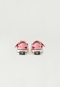 Zapatillas de lona rosas con bordado floral, diseño bajo, suela de goma blanca y clásico logo en blanco y negro en el talón.
