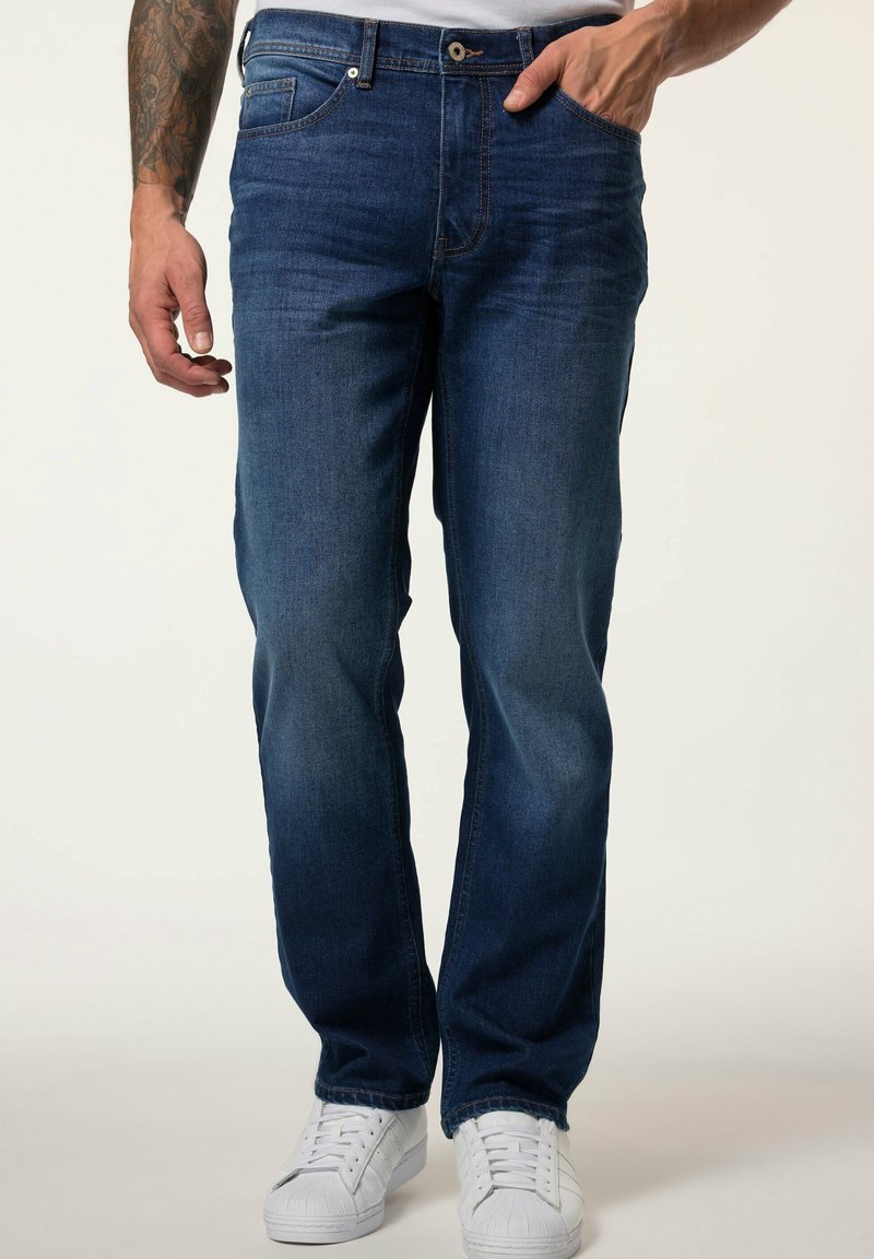 Jeans de mezclilla azul oscuro con corte recto, diseño de cinco bolsillos y un ligero desgastado. Se llevan con zapatillas blancas.
