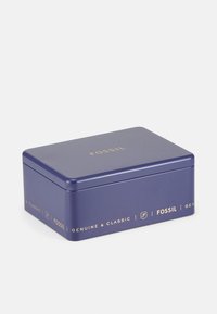 Boîte en métal rectangulaire de couleur violette avec une finition lisse, présentant un texte doré indiquant "FOSSIL" et "GENUINE & CLASSIC" sur les côtés.