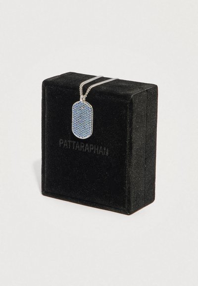 Stříbrný přívěsek ve tvaru známky se stříbrným řetízkem a modrými kameny, umístěný na černé sametové krabičce s nápisem "PATTARAPHAN".