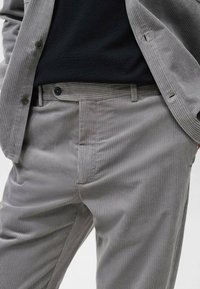 Pantalon en velours côtelé gris avec nervures verticales, doté d'une fermeture à boutons, de poches latérales et d'une coupe droite.
