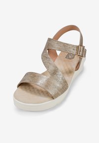 Sandale à talons dorée métallique avec une semelle en caoutchouc, une bride ajustable à la cheville et une semelle intérieure rembourrée. Présente une texture lisse et un design minimaliste.
