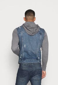 Denimvest med en grå hættetrøje, med en slidt finish, rå kanter og en klassisk pasform. Designet til lag-på-lag styling med et afslappet look.