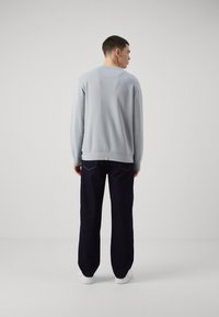 Sudadera azul claro de manga larga, con puños acanalados y un cuello redondeado, combinada con pantalones anchos oscuros y zapatos blancos.