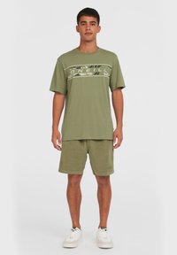 Camiseta de algodón verde olivo con un gráfico floral y un logotipo en el pecho, combinada con pantalones cortos a juego. Diseño casual y de corte relajado.