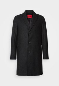 Cappotto nero in lana con vestibilità su misura, rever a punta, chiusura con tre bottoni e tasche laterali. Interno foderato con etichetta del marchio.